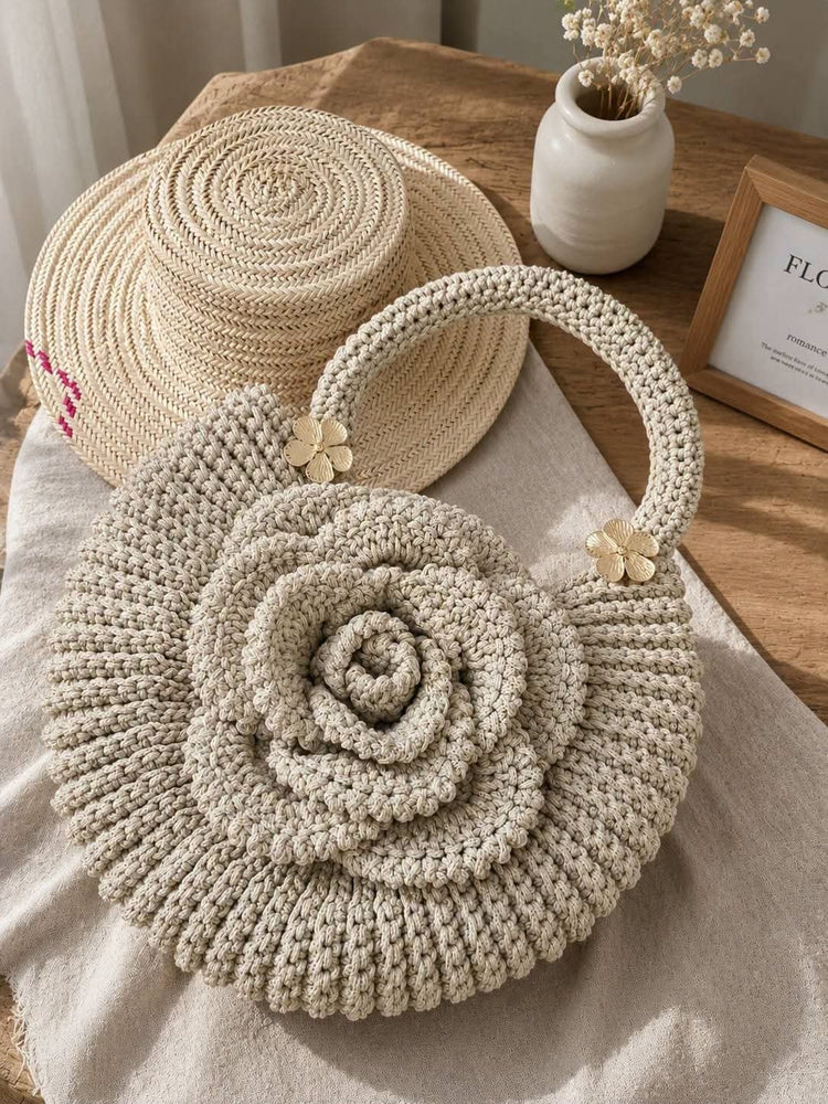 A round, hand-crocheted beige tote bag with a large rose-shaped center and a top handle, styled on a neutral fabric surface next to a matching crocheted straw hat.