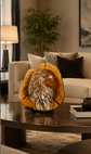 A carved wooden eagle sculpture displayed on a dark round coffee table in a modern living room setting with a sofa, lamp, and plant in the background.

