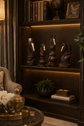 A dark wood built-in shelving unit in a cozy room, displaying four dark carved horse statues on the middle shelf, books and a globe on the top shelf, and a small plant and box on the bottom shelf.

