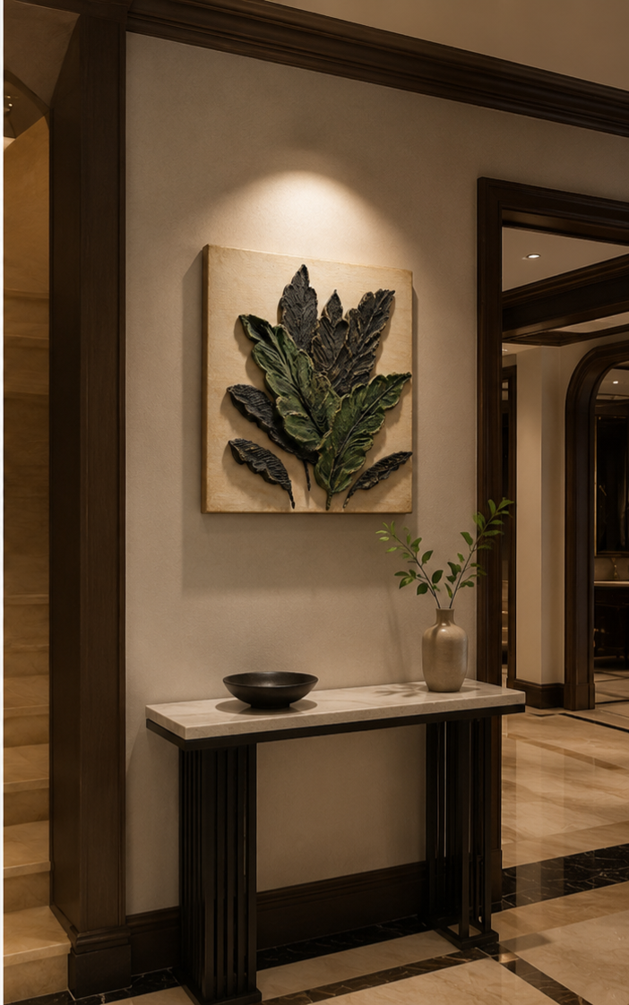 A framed wall art piece featuring a 3D textured green leaf design on a beige background, displayed in a warm, modern hallway above a console table.


